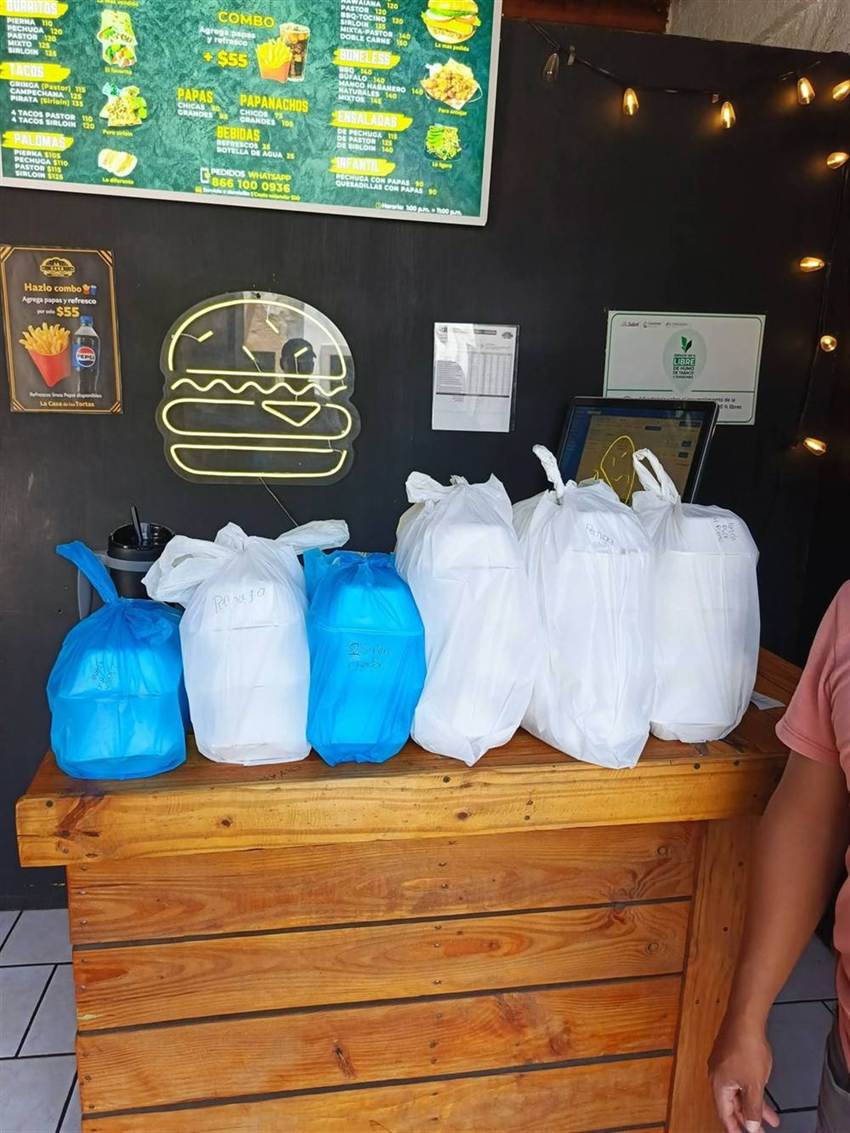 Bolsas de pedidos listos alineadas en el mostrador, cada una etiquetada con su platillo